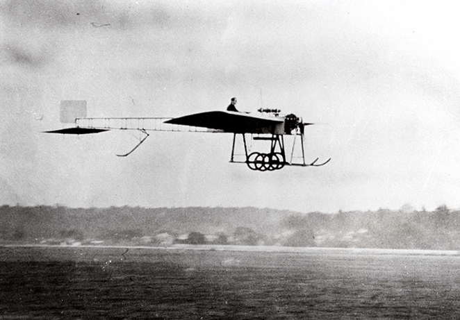 Vintage light monoplane being flown a few meters above thr ground.