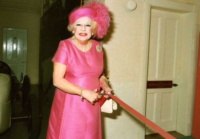 Barbara Cartland in a pink dress cutting a ribbon